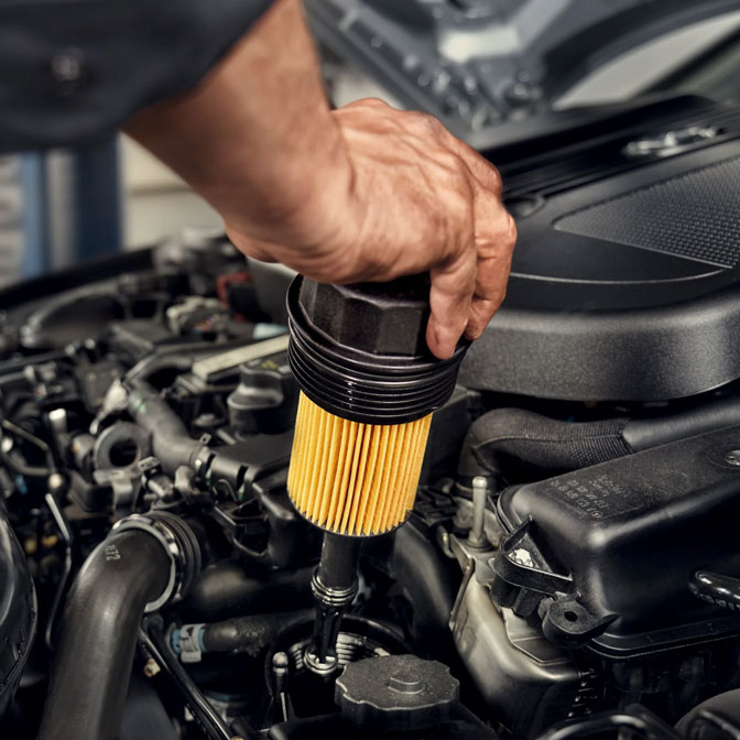 Gezeigt wird ein original Mercedes-Benz Ölfilter, der gerade in den Motorraum eingebaut wird. Gezeigt wird ein original Mercedes-Benz Ölfilter, der gerade in den Motorraum eingebaut wird.